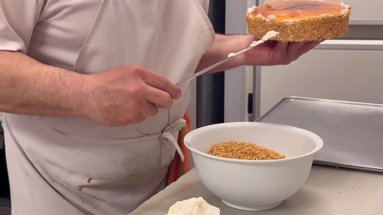 Nahaufnahme der Hände eines spanischen Konditors, der in seiner Konditorei einen Kuchen zubereitet und mit den Händen zerstoßene Mandeln hinzufügt.