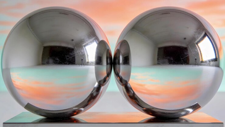 Camera recording two chrome spheres reflecting window on mirror base in studio, documenting display