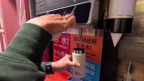 person using hot water dispenser with own cup