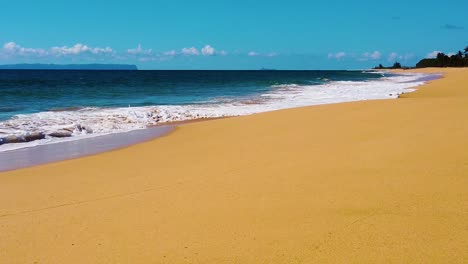 hd hawaii kauai slow motion low trucking in with beach along bottom toward frame right with ocean waves crashing in from left to right with an island in the distance and clouds on the horizon