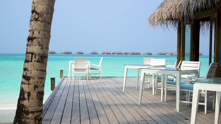 sedie a sdraio bianche al ristorante del resort delle maldive sull'acqua con bungalow sull'acqua sullo sfondo