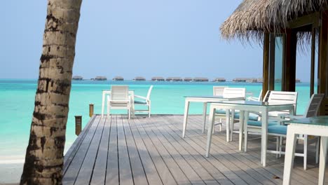 white deck chairs at maldives resort restaurant by the water with overwater bungalows in the background