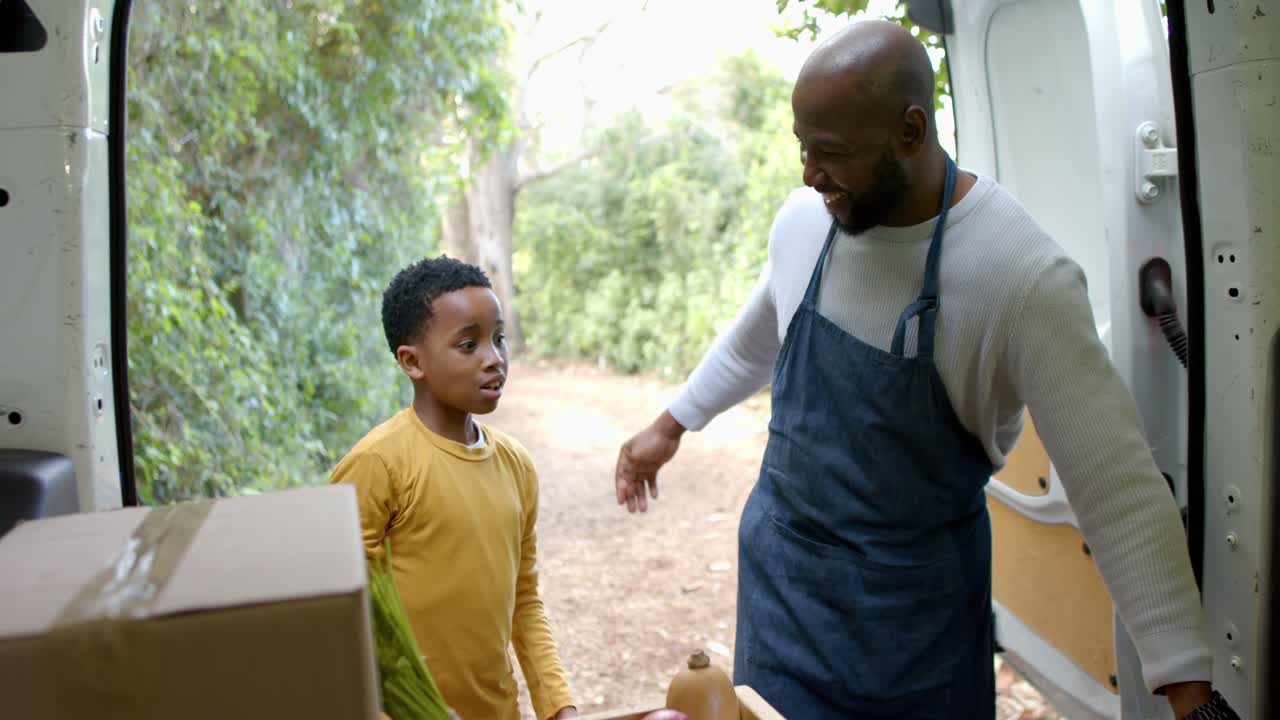 African American father and son by van exchanging high fives bumping fists while learning produce