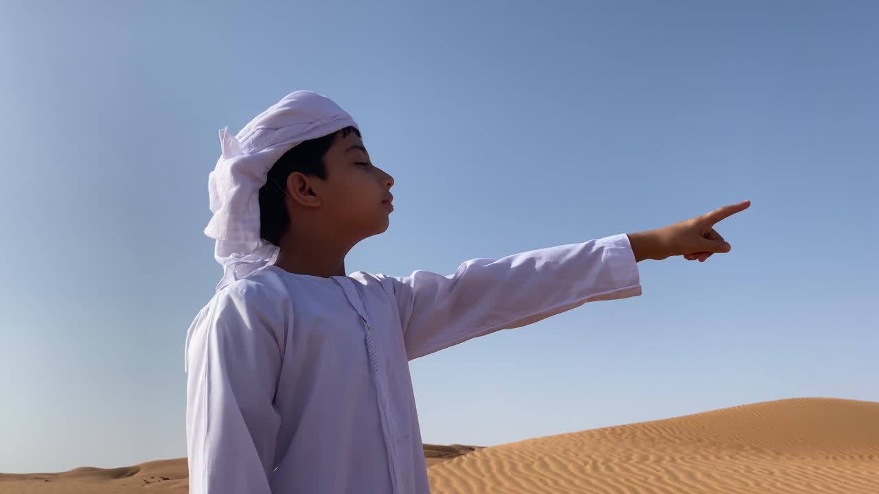 emarati niño señalando a un lugar lejano en el desierto