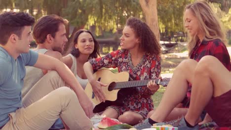 mujer hipster tocando la guitarra en el parque con sus amigos