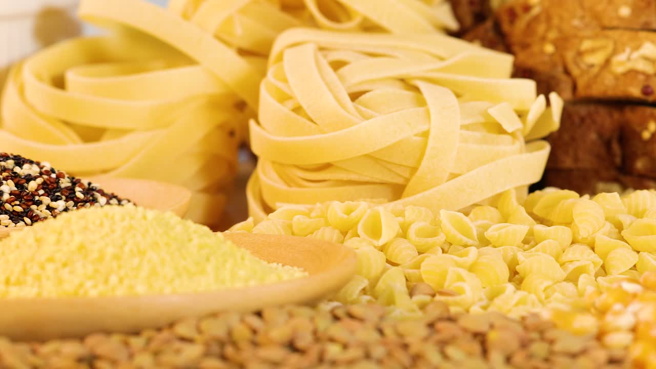 A variety of grains and pasta displayed in warm lighting, highlighting textures and colors in a close-up composition