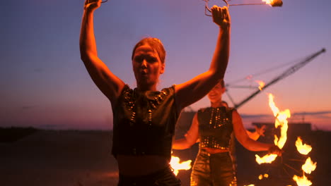 professional artists show a fire show at a summer festival on the sand in slow motion. fourth person acrobats from circus work with fire at night on the beach