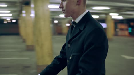 Young-man-in-a-suit-with-bow-tie-moving-shopping-cart-to-his-black-car-in-the-parking-at-night