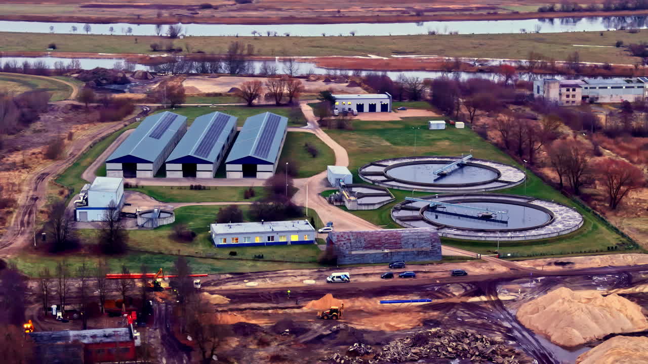 Aerial view of a modern agricultural facility with barns and circular water treatment tanks in a rural landscape