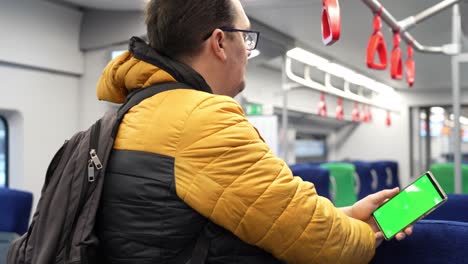 vista trasera de un hombre mirando un teléfono inteligente con pantalla verde y navegando en línea en el tren. maquillaje para ver contenido en el teléfono celular. teléfono digital en blanco en la mano de un tipo de pie en el interior en el transporte público. imágenes de alta calidad 4k