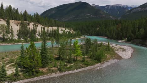 Aufsteigender-Drohnenschuss-Mit-Blick-Auf-Den-Unberührten-Und-Sauberen-Kootenay-Fluss-Mit-Bergen-Und-Einem-Kleinen-Waldbrand-Im-Hintergrund