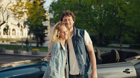 A-young-beautiful-couple-of-a-brunette-guy-and-a-blonde-girl-are-standing,-posing-and-looking-at-the-camera-against-the