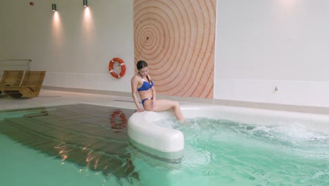 attractive woman in bikini sits on edge of bubbling heated hotel pool