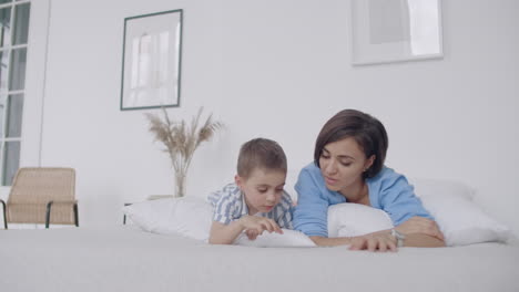 madre e hijo usando tableta digital en el dormitorio en casa. vista frontal de madre y hijo caucásicos felices usando tableta virtual en el dormitorio en casa
