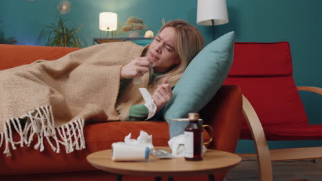 sick ill young woman suffering from cold, allergy lying on home sofa sneezes wipes snot into napkin