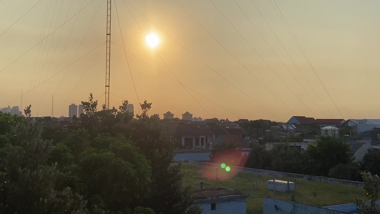 Puesta de sol cálida y dorada sobre un paisaje urbano con una torre de comunicaciones