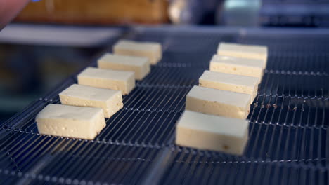 white creamy sweets being laid on the conveyor grate by the worker's hands in gloves. candies move quickly on the conveyor to go under the next procedure. close up.