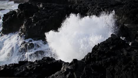 wave crashing on dark black basalt rock shore of volcanic island