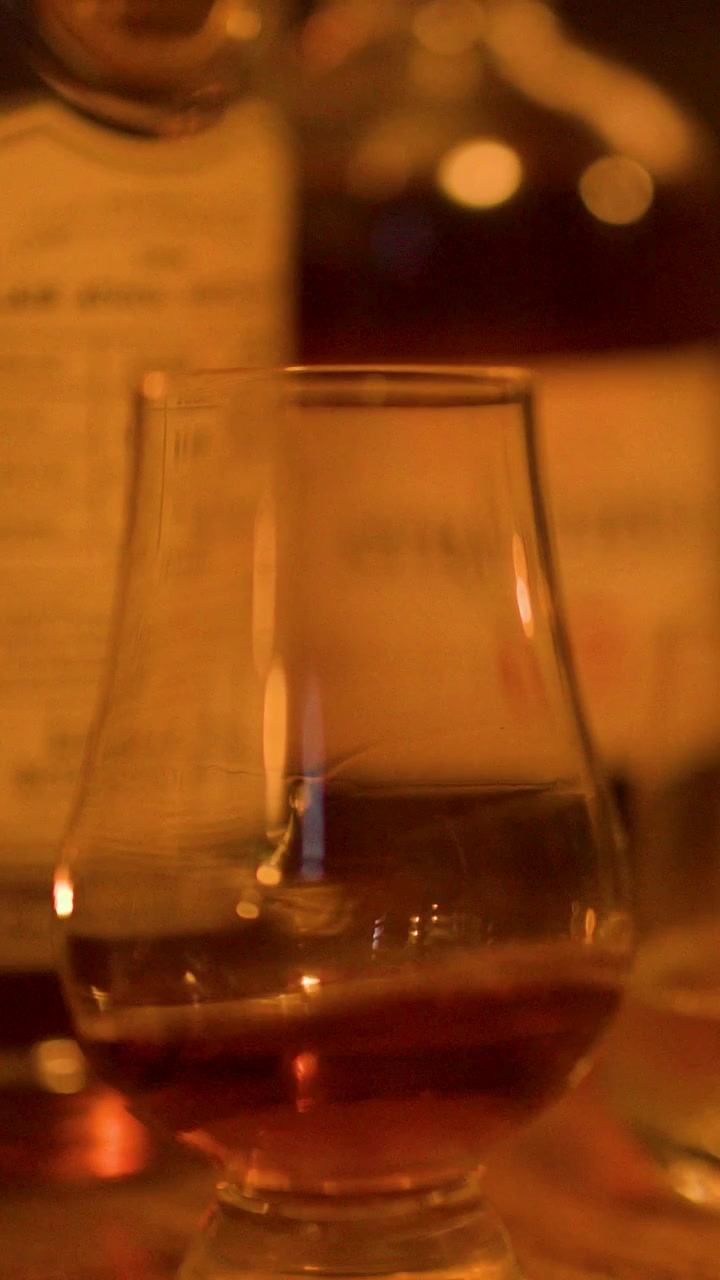 Primo piano di un bicchiere di whisky fatto roteare a mano, bevanda ambrata, illuminazione serale calda, bar.