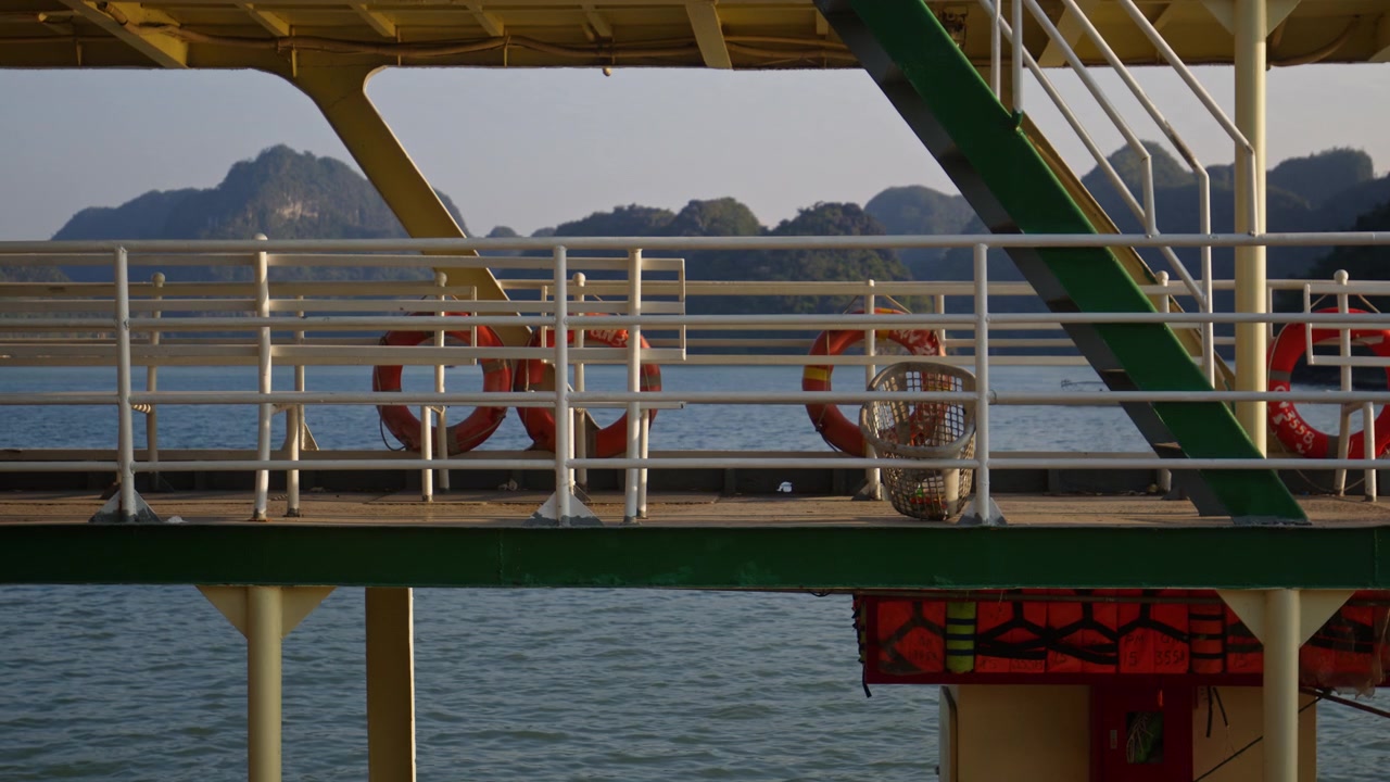 Traghetto passeggeri roll-on/roll-off con panchine metalliche vuote su un ponte all'aperto che naviga oltre montagne calcaree nella Baia di Ha Long