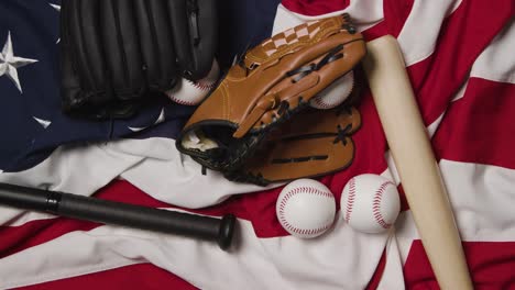 overhead baseball still life with bat and catchers mitt on american flag with ball rolling into frame 3