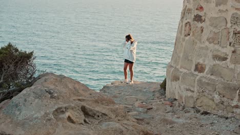 una joven atractiva posando con confianza en las rocas del acantilado al atardecer