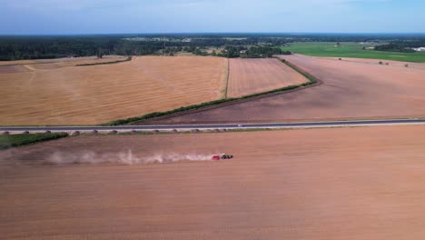 Sideview-of-tractor-ploughing-across-dry-field-next-to-highway-in-midday