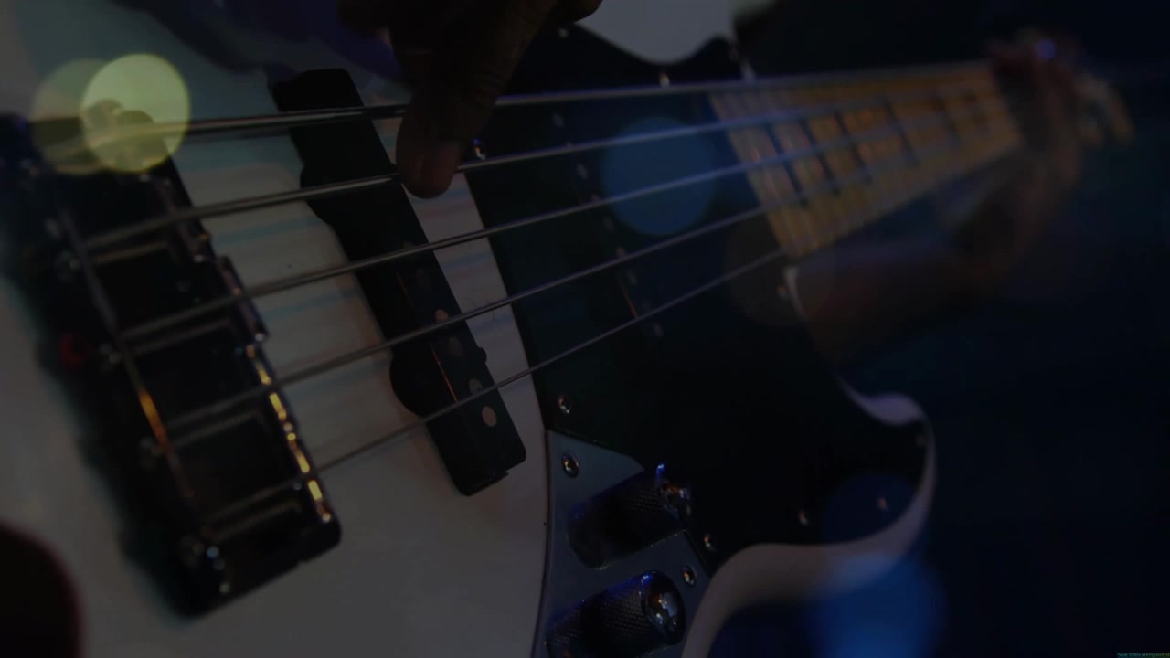 La mano destra di un musicista che pizzica e fa scorrere la corda del Mi basso, creando un groove durante un'esibizione di musica dal vivo sotto le luci.