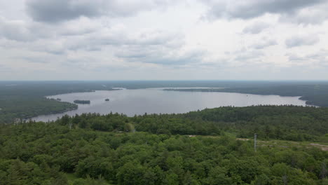 aerial shot over green tree covered mountain past radio tower towards lake calabogie on a cloudy day. ontario canada