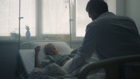 pediatrician examining little patient in hospital ward. girl lying in clinic bed