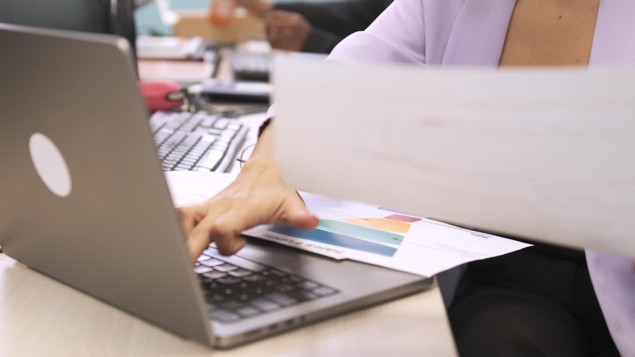Businesswoman using laptop while analyzing data on documents in office