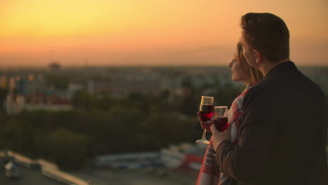 Mann-Und-Junge-Hübsche-Frau-Sitzen-Auf-Der-Couch,-Halten-Weingläser-Und-Küssen-Sich-Bei-Sonnenuntergang-Auf-Der-Dachterrasse