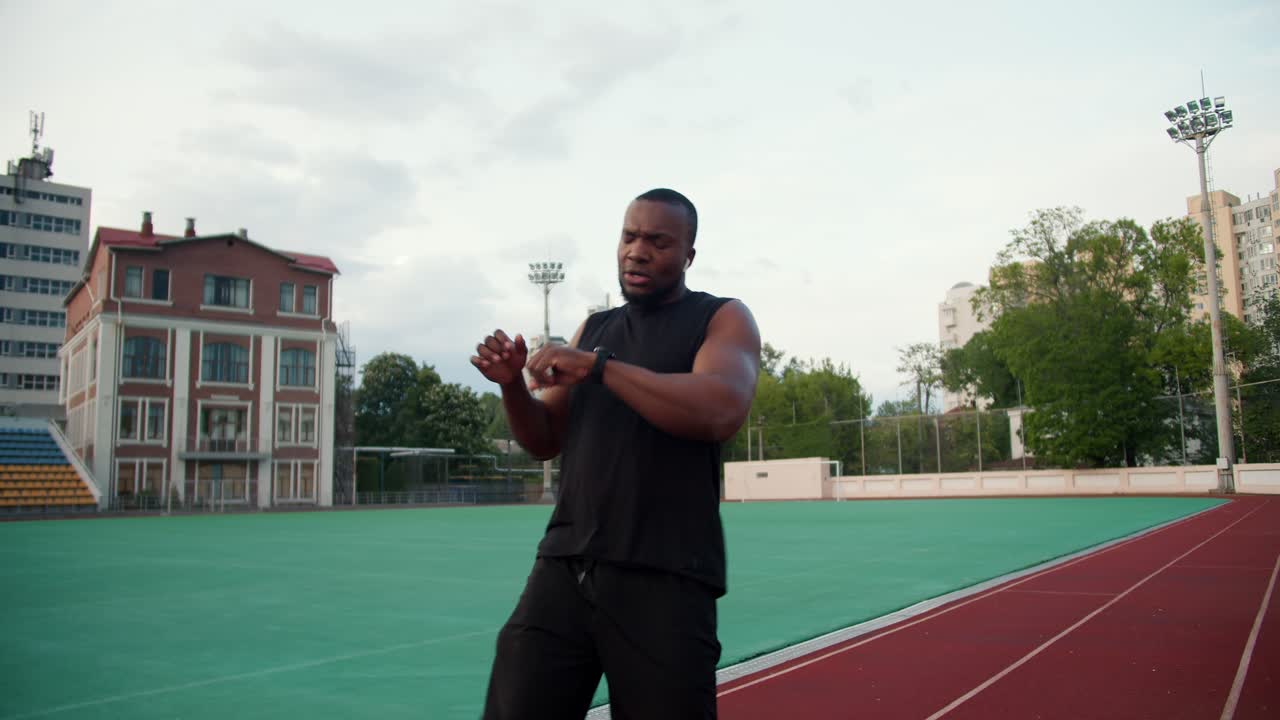 A Black-skinned man in black sportswear runs a speed race after which he looks at the time and rests