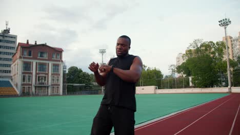 a black-skinned man in black sportswear runs a speed race after which he looks at the time and rests