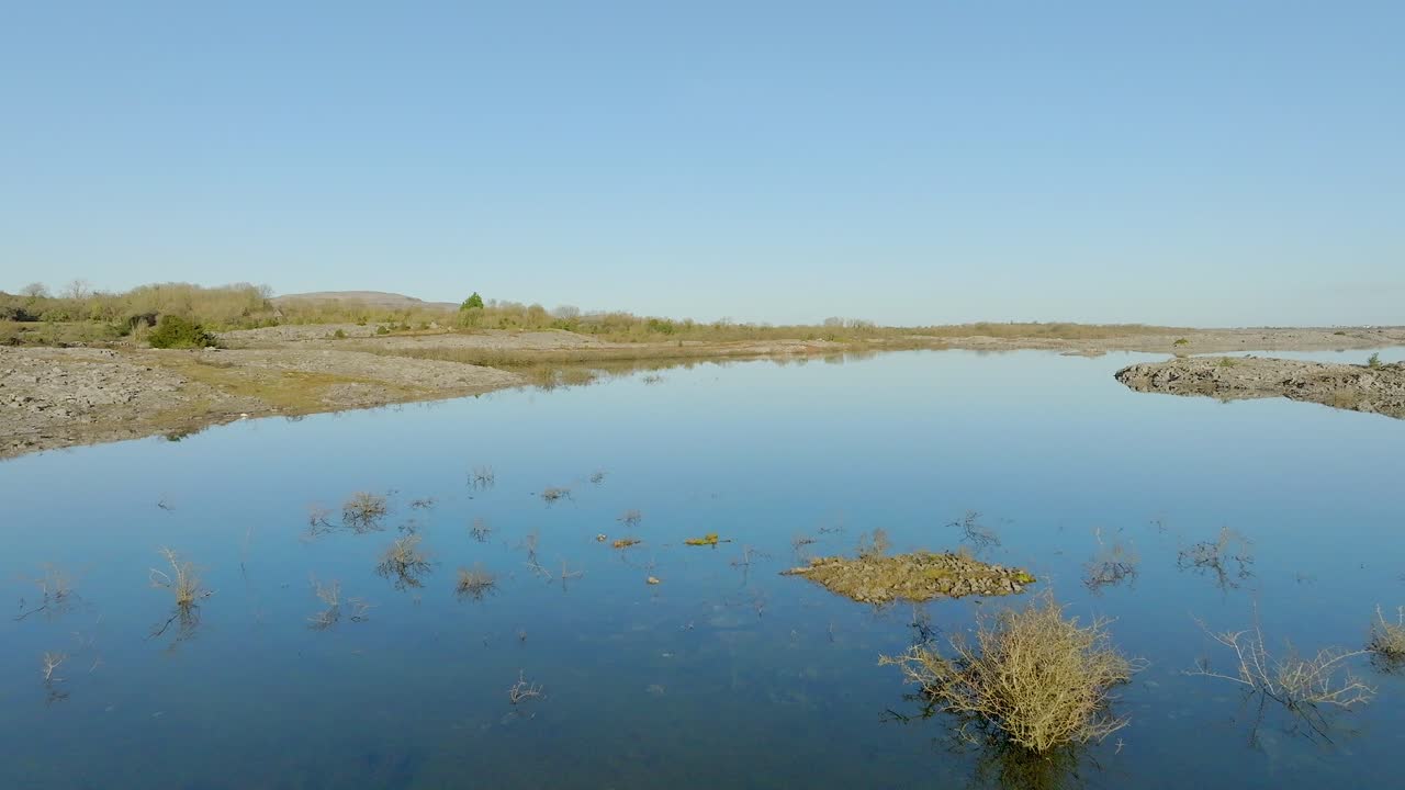 lenta carreta aérea sobre ramas de arbustos en aguas de inundación poco profundas que reflejan el cielo azul en un día soleado en la irlanda de burren