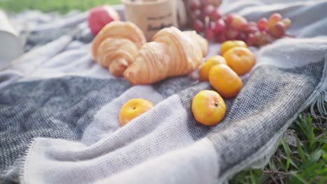 romantic picnic on a blanket of gray with apples, grapes, mandarins, croissants and fruits in a straw bag on the beach