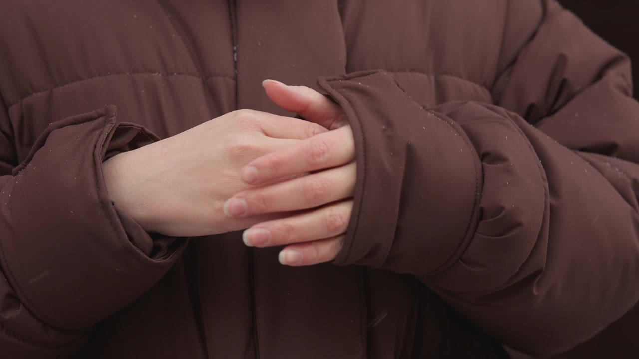 Tight chest-level view of person in brown quilted puffer coat fastening closure with both hands, adjusting sleeve cuffs, then folding arms across chest in calm winter prep, with hand, coat, puffer