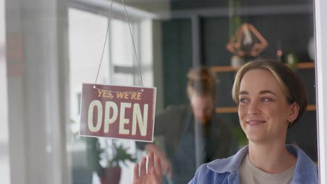 Sonriente-Peluquera-Caucásica-Girando-El-Cartel-De-La-Tienda-Para-Abrir-La-Puerta-De-La-Peluquería,-En-Cámara-Lenta