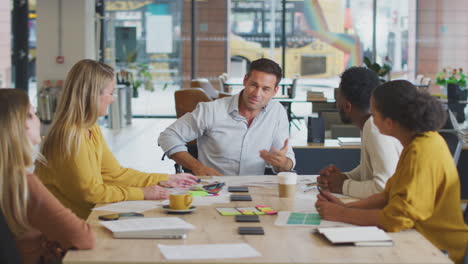 businessman in wheelchair gives presentation to colleagues around table in modern open plan office