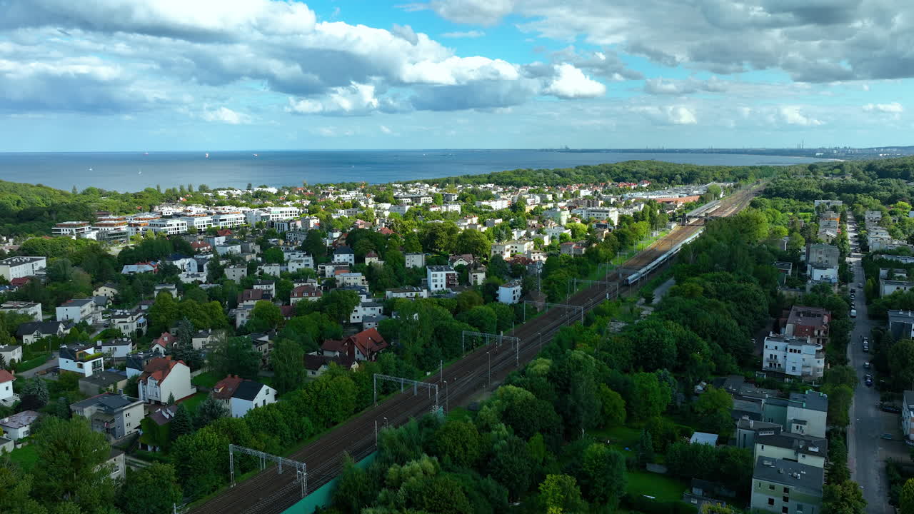 gdynia orłowo의 공중 사진, 풍요로운 초록색으로 둘러싸인 주거 지역을 보여주는, 철도 노선과 발트해를 배경으로