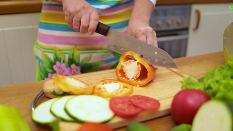 female hands of housewife with a knife cut fresh bell pepper on chopping board kitchen table