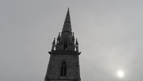 aerial view rising tilt down of decorative medieval stone church tower steeple against overcast sky