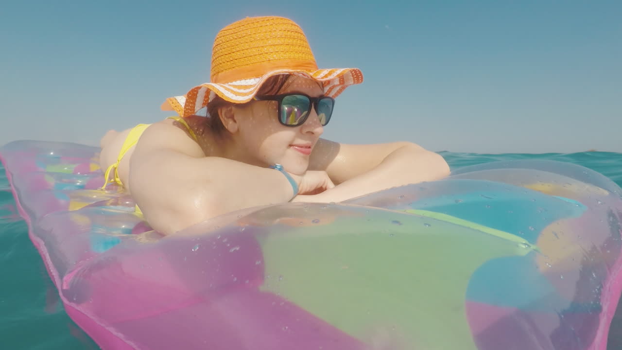 Attractive Woman In An Orange Hat Floats In The Sea On An Inflatable Mattress