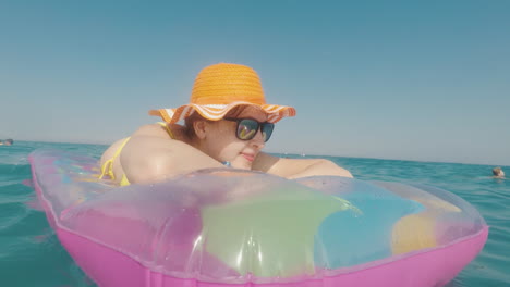 mujer atractiva con un sombrero naranja flota en el mar sobre un colchón inflable