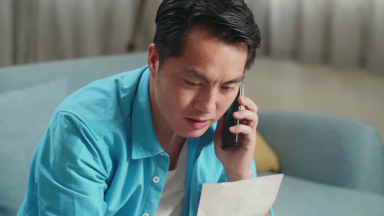 노트북을 들고 있는 아시아인 남자가 전화에 응답하고 손에 든 청구서를 보면서 행복해진다.