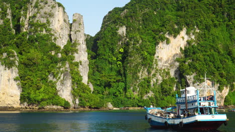 local boat floating near massive vegetated karst mountains, thailand