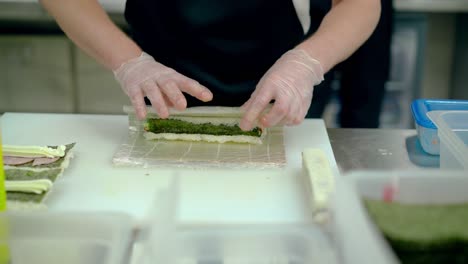 Cook-prepares-Japanese-rolls-with-Bulgarian-pepper-cucumber-wraps-with-a-mat-in-boiled-rice-and-seaweed-nori