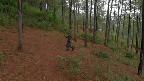 Toma-Aérea-En-Cámara-Lenta-De-Un-Cazador-Africano-Cazando-En-Un-Bosque-Y-Disparando-Una-Flecha-Desde-Un-Arco