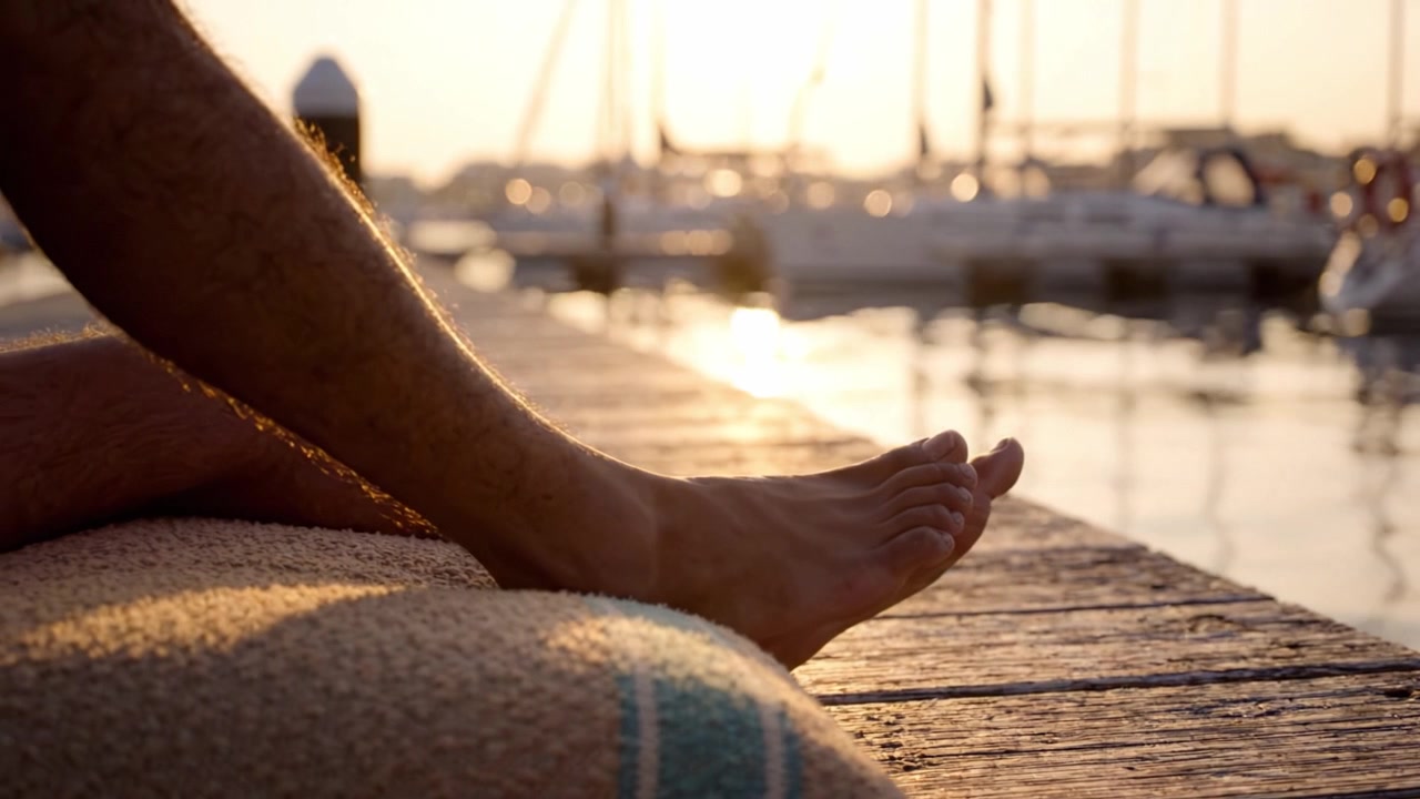 Un Tramonto Sereno su Acque Tranquille con i Piedi che si Rilassano su un Molo, Catturando l'Essenza di Momenti Sereni al Porto, Immersi nella Luce Dorata.