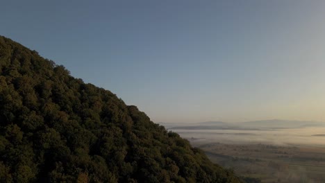 Slow-flight-around-forest-covered-hill-at-edge-of-vast-flat-lands